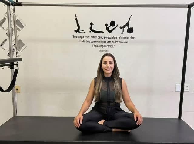Gabriela sentada no Cadillac, diante da parede do estúdio com a frase de Joseph Pilates